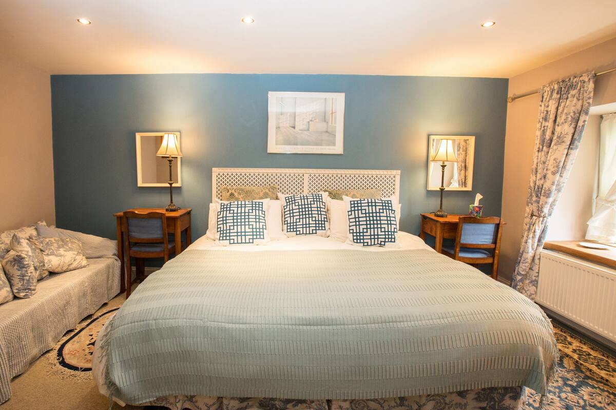 A neatly arranged bedroom with a large bed, two bedside tables with lamps, a small desk, and a chair.