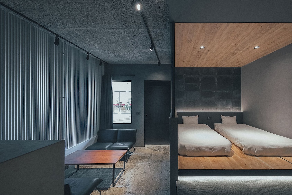 A modern bedroom with two beds, a desk, and a seating area.