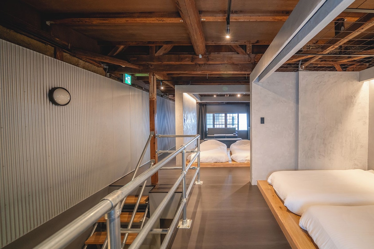 A hotel room with a wooden ceiling, a bed with white bedding, a window with a view, and a staircase with metal railings.