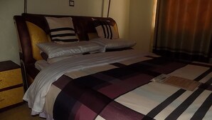 A neatly made bed with a striped bedspread, a wooden headboard, and multiple pillows. - Country Motel Koboko (Koboko)