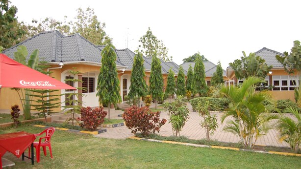 A courtyard with a Coca-Cola branded umbrella, a red chair, and a paved walkway. - Country Motel Koboko (Koboko)