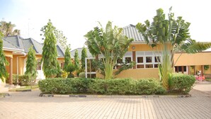 A building with a tiled roof, surrounded by well-maintained greenery and a paved walkway. - Country Motel Koboko (Koboko)