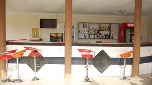 A bar area with stools, a Coca-Cola refrigerator, and a shelf with various bottles. - Country Motel Koboko (Koboko)