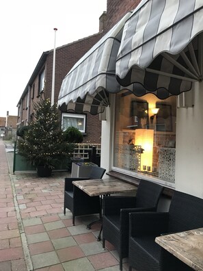 An outdoor seating area with wicker furniture, a Christmas tree, and a building with a striped awning. - Hotel Valkenhof (Zoutelande)
