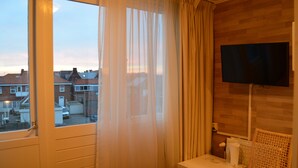 A hotel room with a large window, a television on the wall, and a wooden floor. - Hotel Valkenhof (Zoutelande)