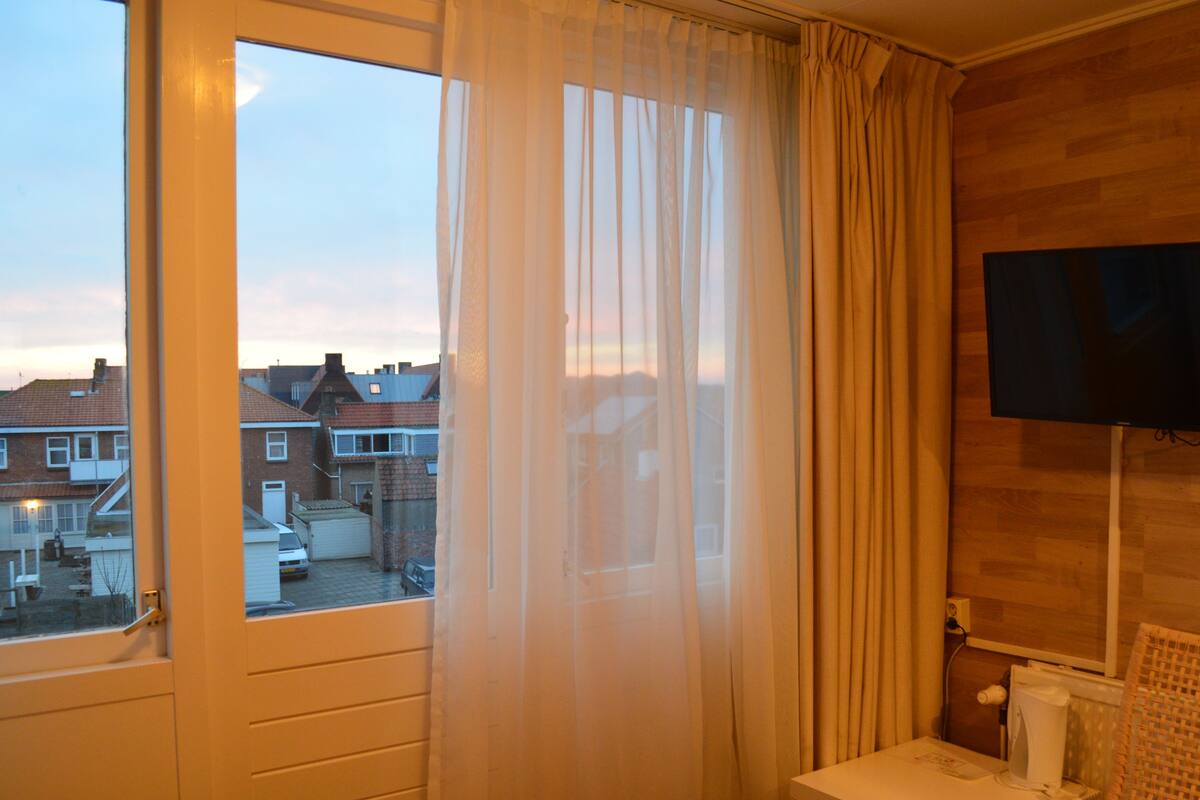 Ein Hotelzimmer mit großem Fenster, einem an der Wand befestigten Fernseher und Holzboden.