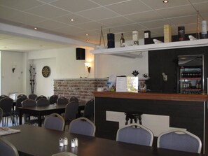 A restaurant with a brick wall, a counter with various items, and several tables and chairs. - Hotel Valkenhof (Zoutelande)
