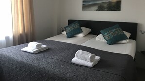 A neatly made bed with two pillows, a folded towel, and a painting of a beach scene on the wall. - Hotel Valkenhof (Zoutelande)
