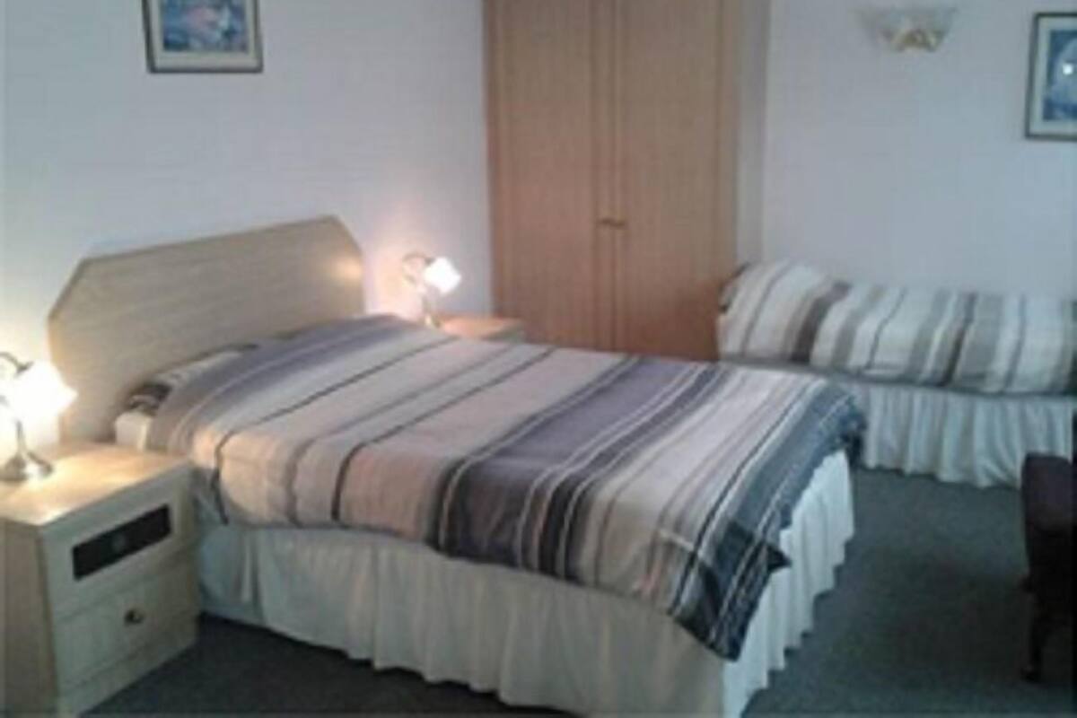 A bedroom with a bed, nightstand, wardrobe, and a small table with a lamp.