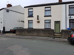 A two-story residential building with a white exterior and a stone wall in front. - Overnight Stays Stockport (Stockport)