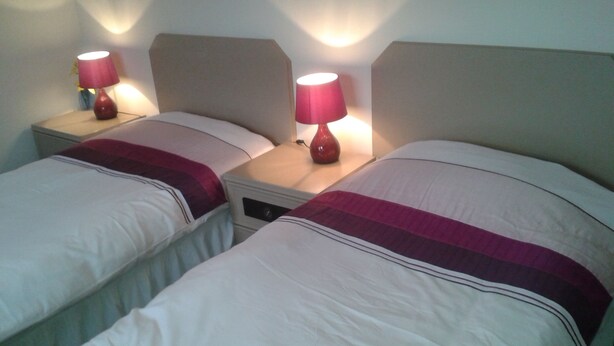 Two single beds with headboards, each with a bedside table and a lamp. - Overnight Stays Stockport (Stockport)