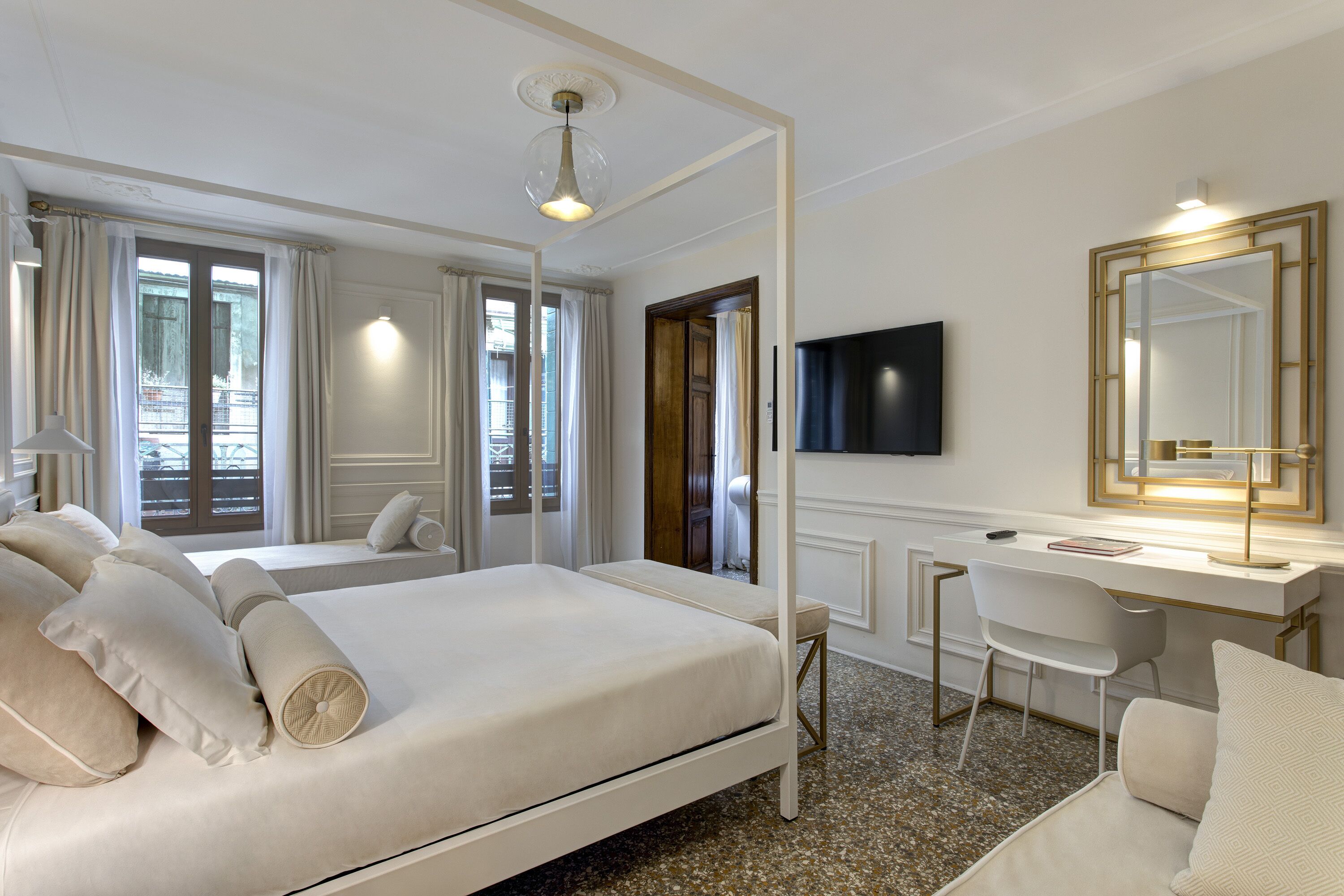 Habitación de hotel con una cama grande, un escritorio, una silla, un televisor y un espejo amplio.