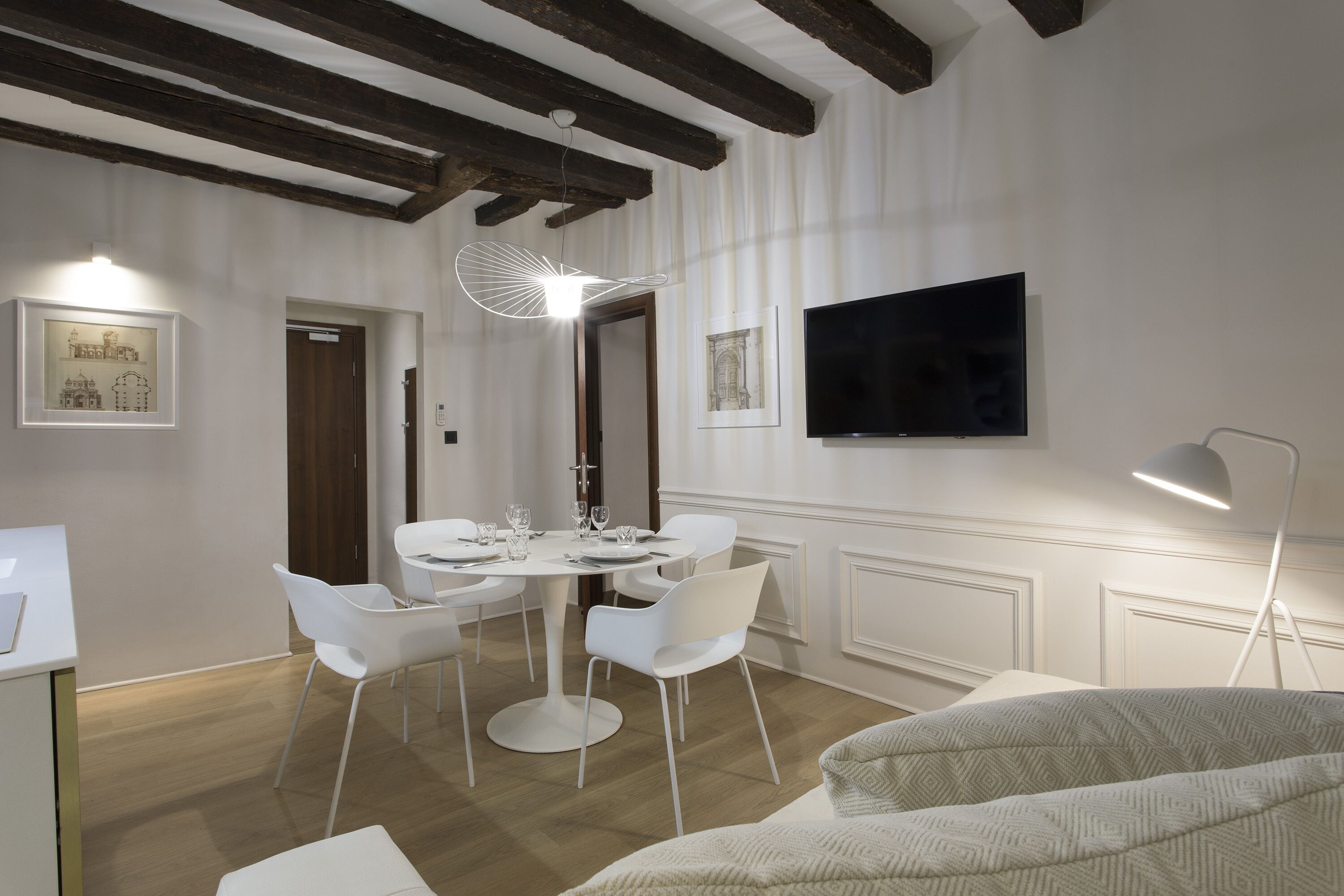 A dining area with a round table, white chairs, a flat-screen TV, and a pendant light.