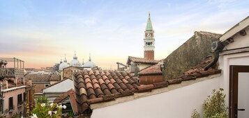 Panoramica di una città con tetti in terracotta, una chiesa con un campanile alto e strutture a cupola in lontananza.