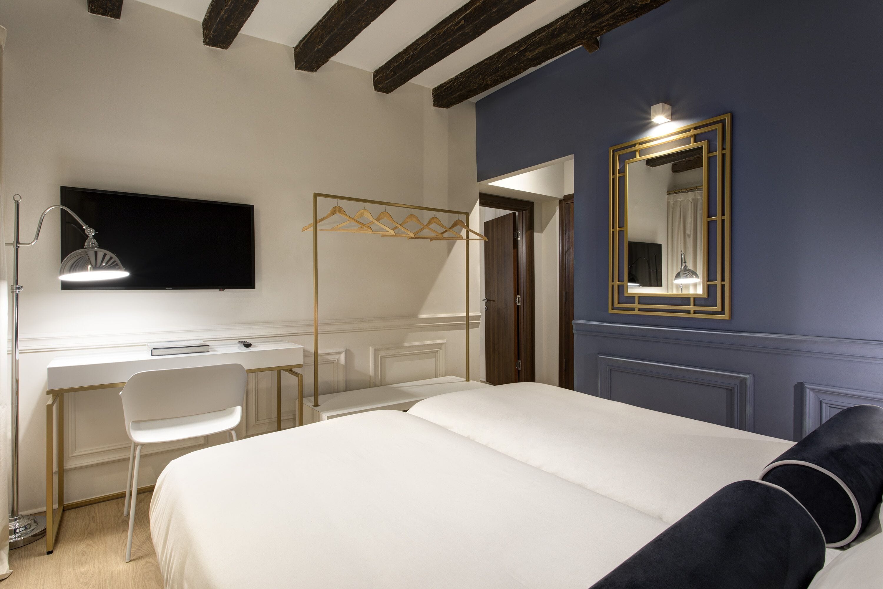 A bedroom with a bed, a desk, a chair, a TV, and a mirror.