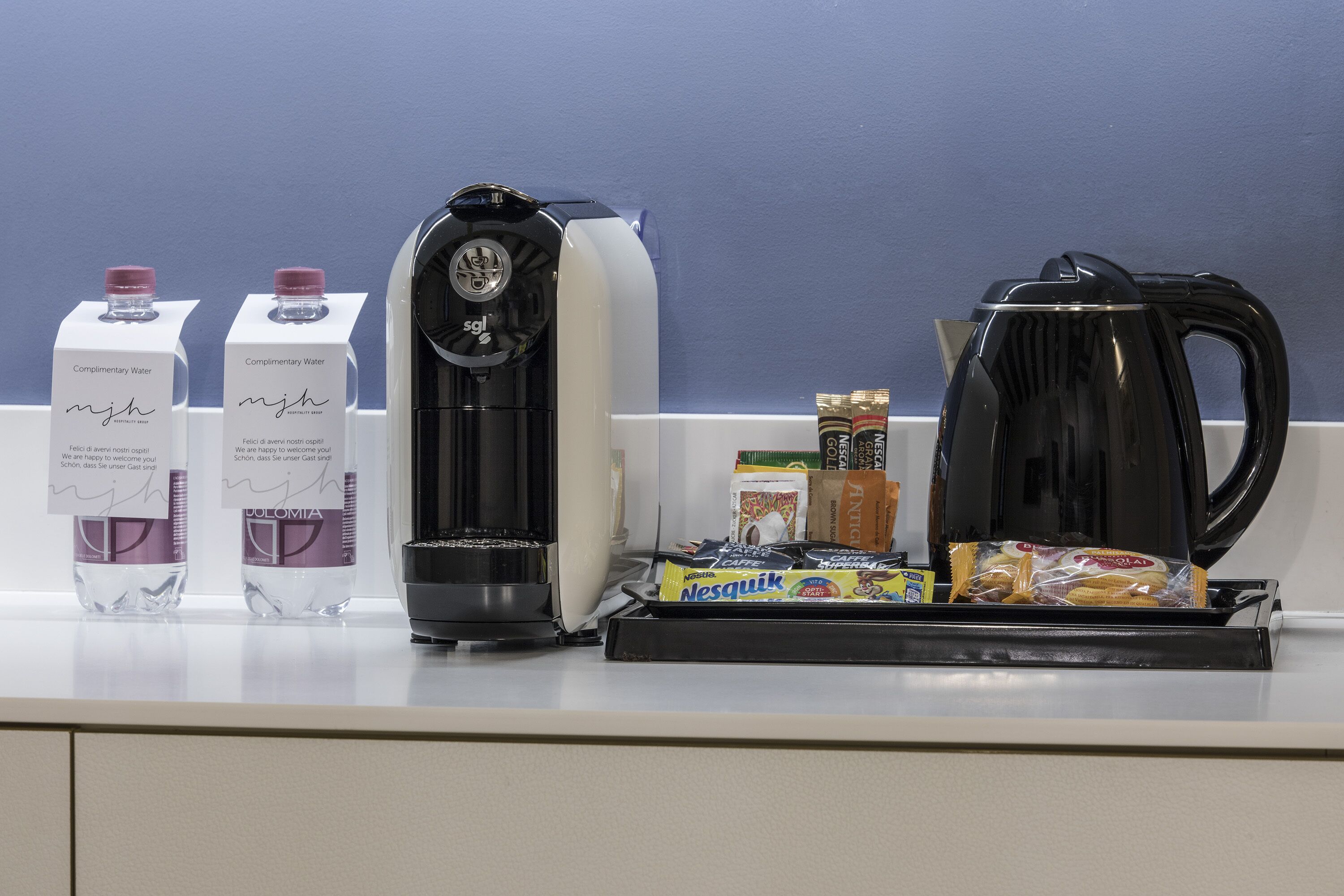 Een koffiehoek met een koffiezetapparaat, twee waterdispensers en een dienblad met koffiecups en snacks.