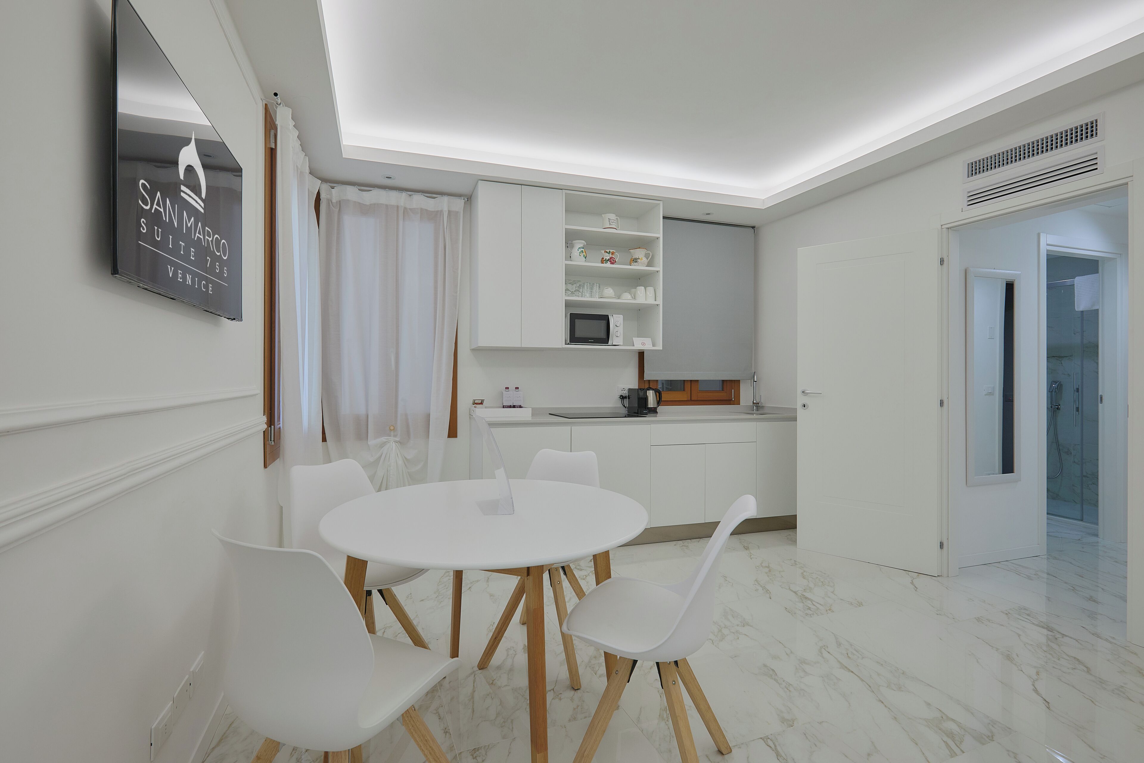 Una cocina moderna con armarios blancos, una mesa redonda con sillas y un microondas integrado.