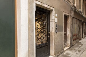 Un edificio con un numero civico, un cancello metallico e una porta con un piccolo oblò.