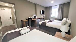 A hotel room with two beds, a desk with a microwave, a TV, and a window with curtains. - The New County Hotel (Gloucester)