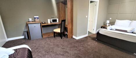 A hotel room with a bed, a desk with a chair, a microwave, and a small refrigerator.