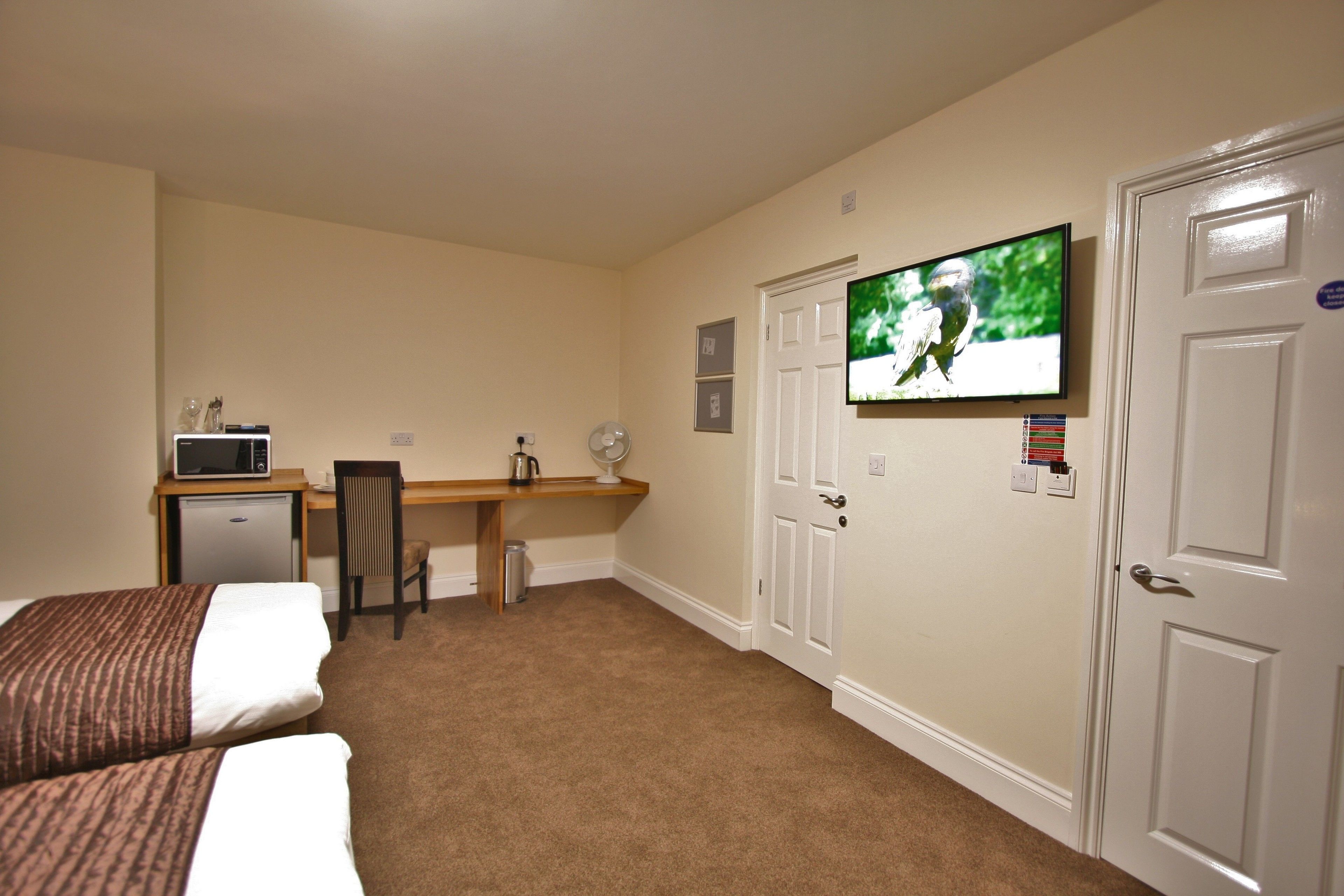 A hotel room with two beds, a desk with a microwave, a chair, a television, and a door.