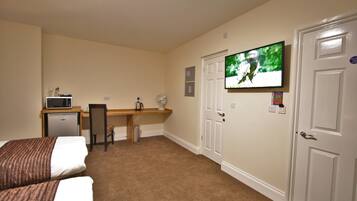 A hotel room with two beds, a desk with a microwave, a chair, a television, and a door.