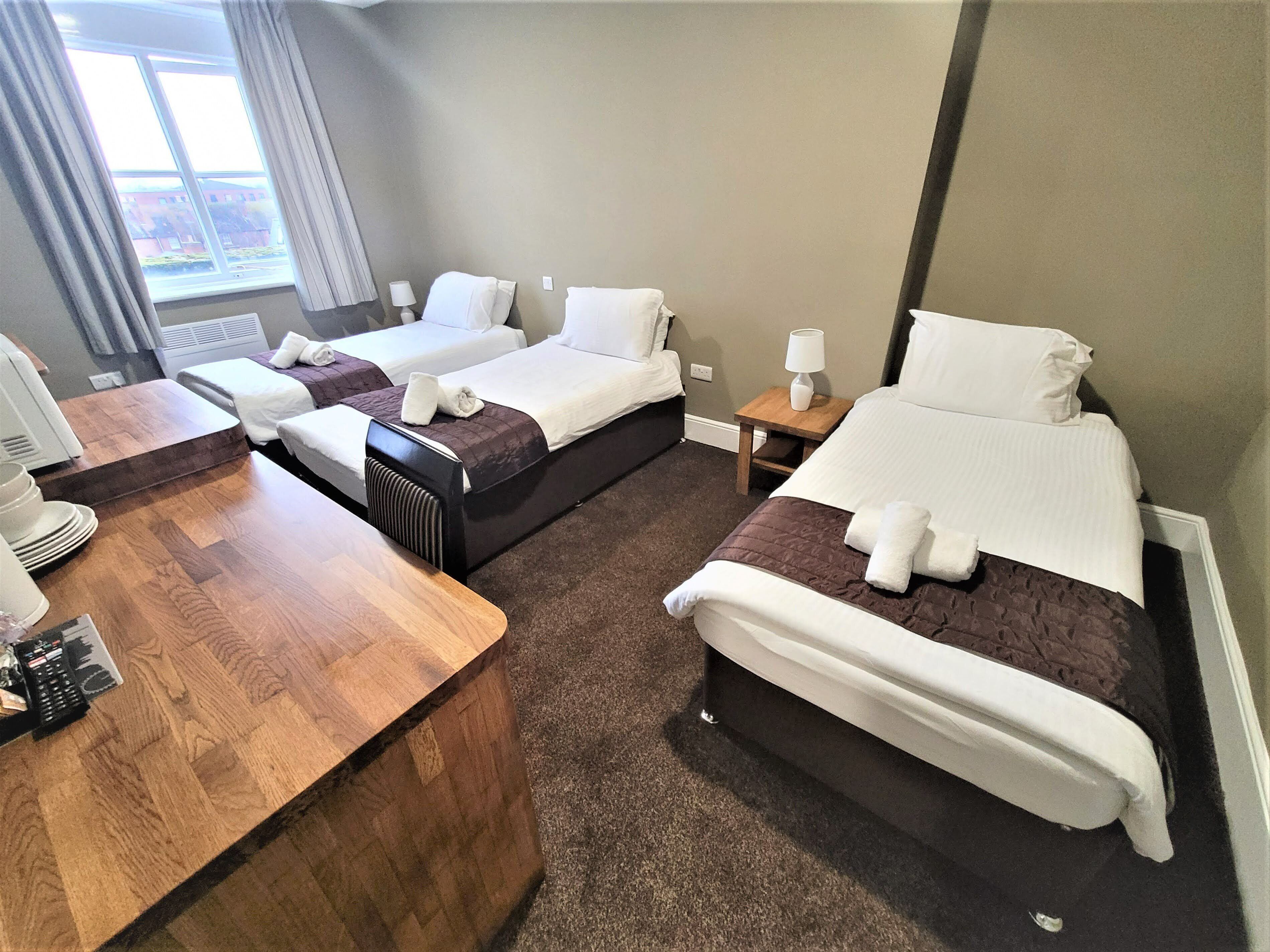 A hotel room with two beds, a wooden desk with a telephone, and a window with curtains.