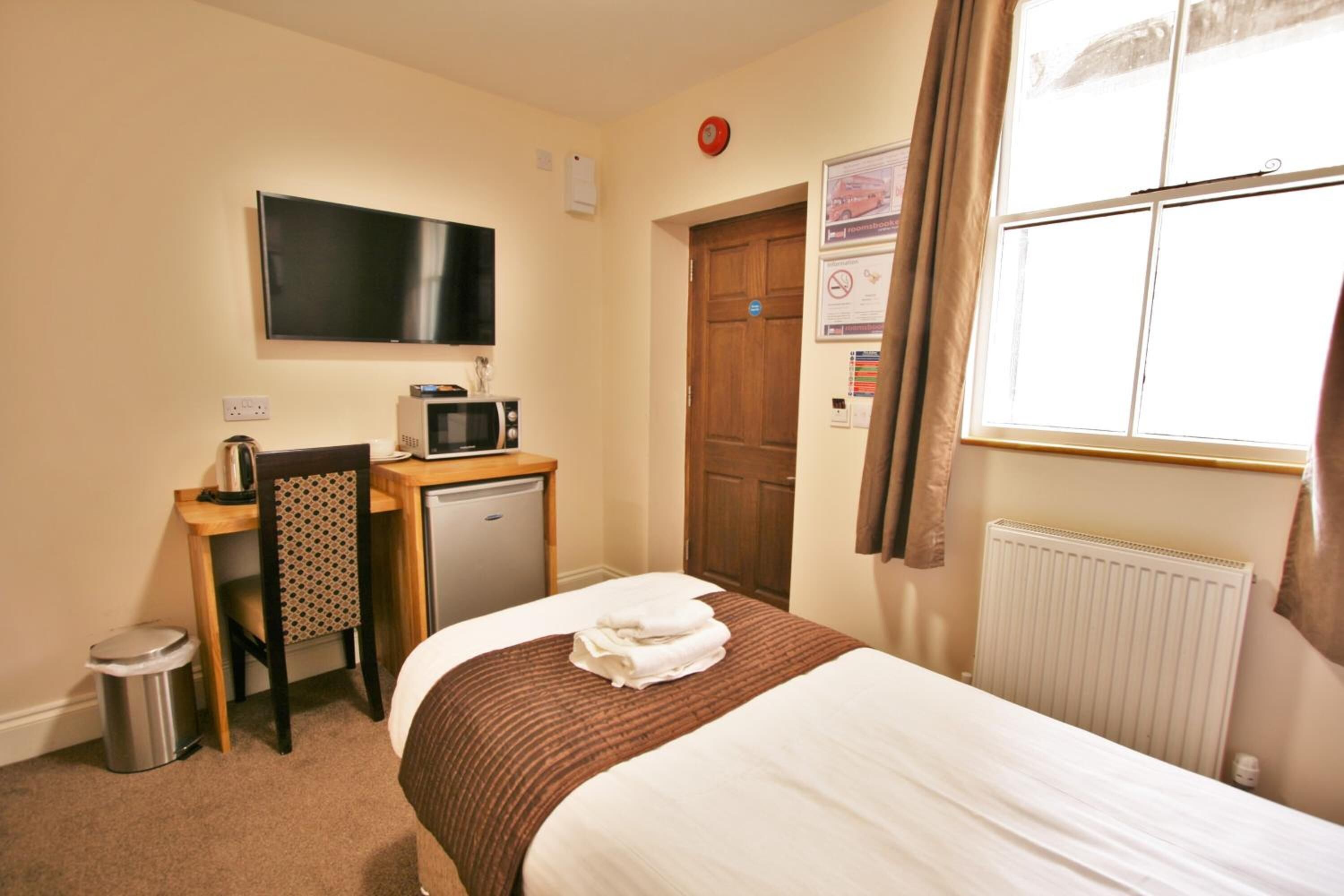 A hotel room with a bed, a desk with a microwave, a TV, and a radiator.