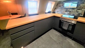 A modern kitchen with a wooden countertop, built-in appliances, and a stone backsplash. - The New County Hotel (Gloucester)