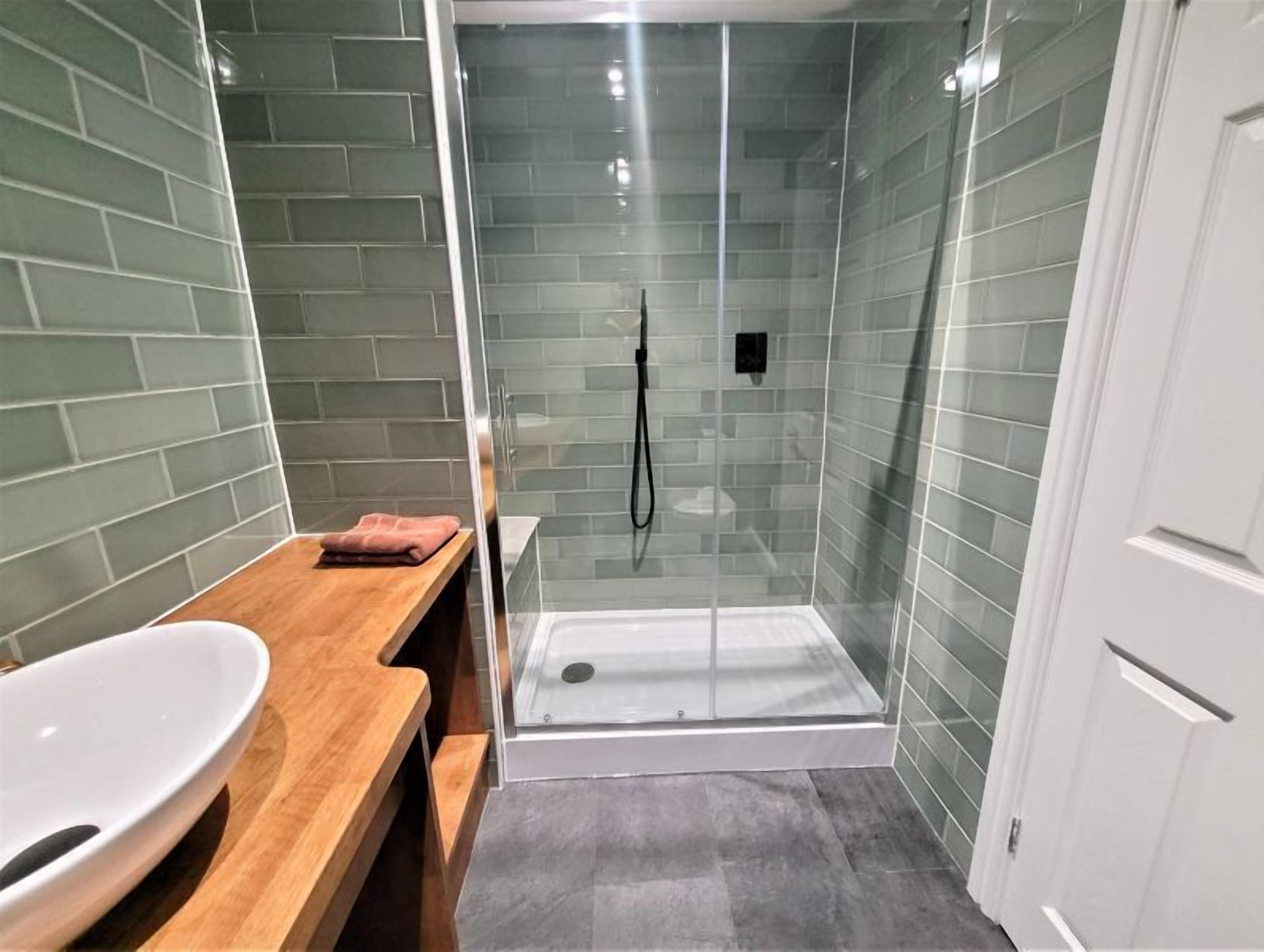 A bathroom with a glass-enclosed shower, a wooden vanity, and a white sink.