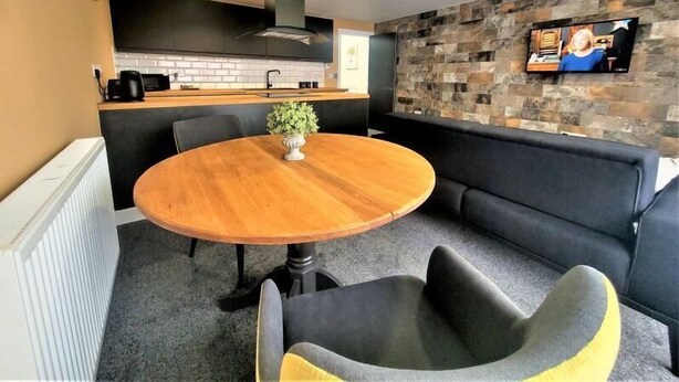 A modern kitchen with a black countertop, a round wooden table, and a black sofa. - The New County Hotel (Gloucester)