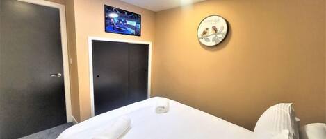 Una habitación de hotel con una cama, una lámpara en el techo, una puerta y un reloj de pared.