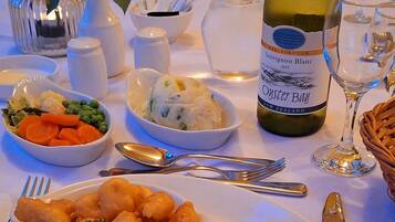 Una mesa de comedor servida con platos de comida, una botella de vino y varios utensilios.