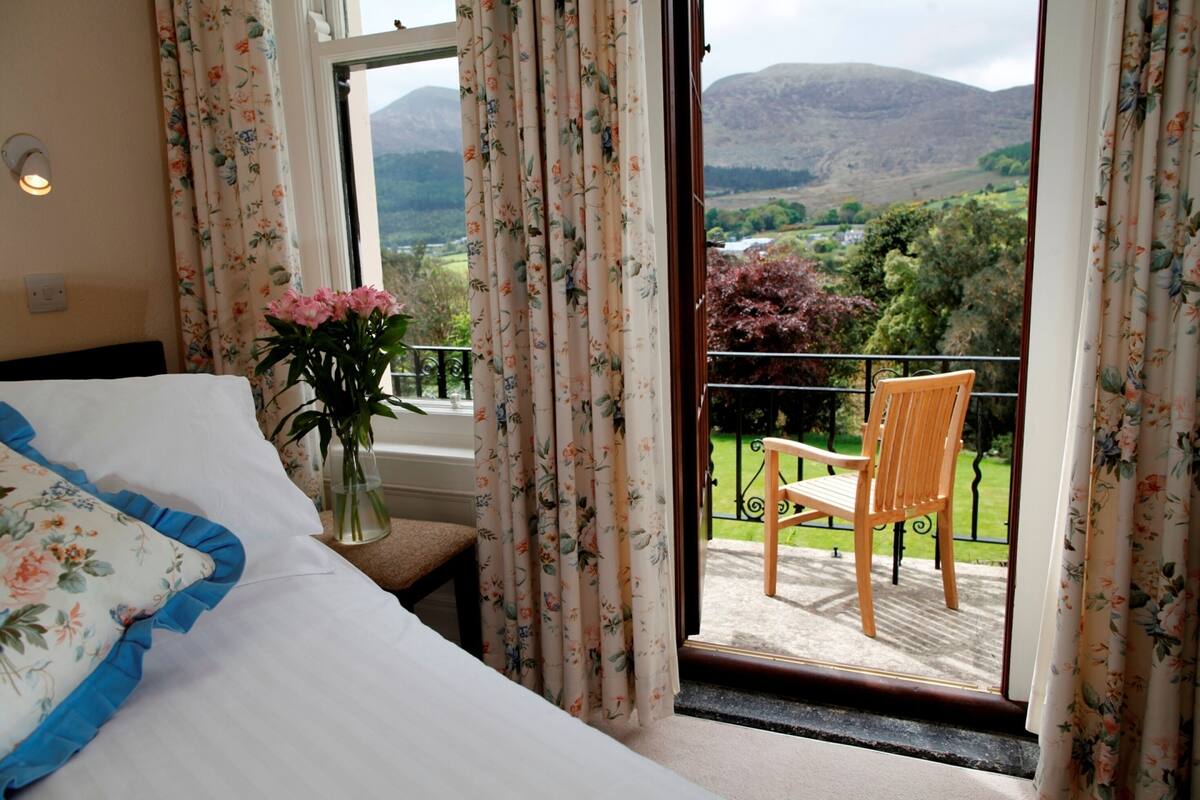 A bedroom with a bed, a vase with flowers, and a balcony with a chair.