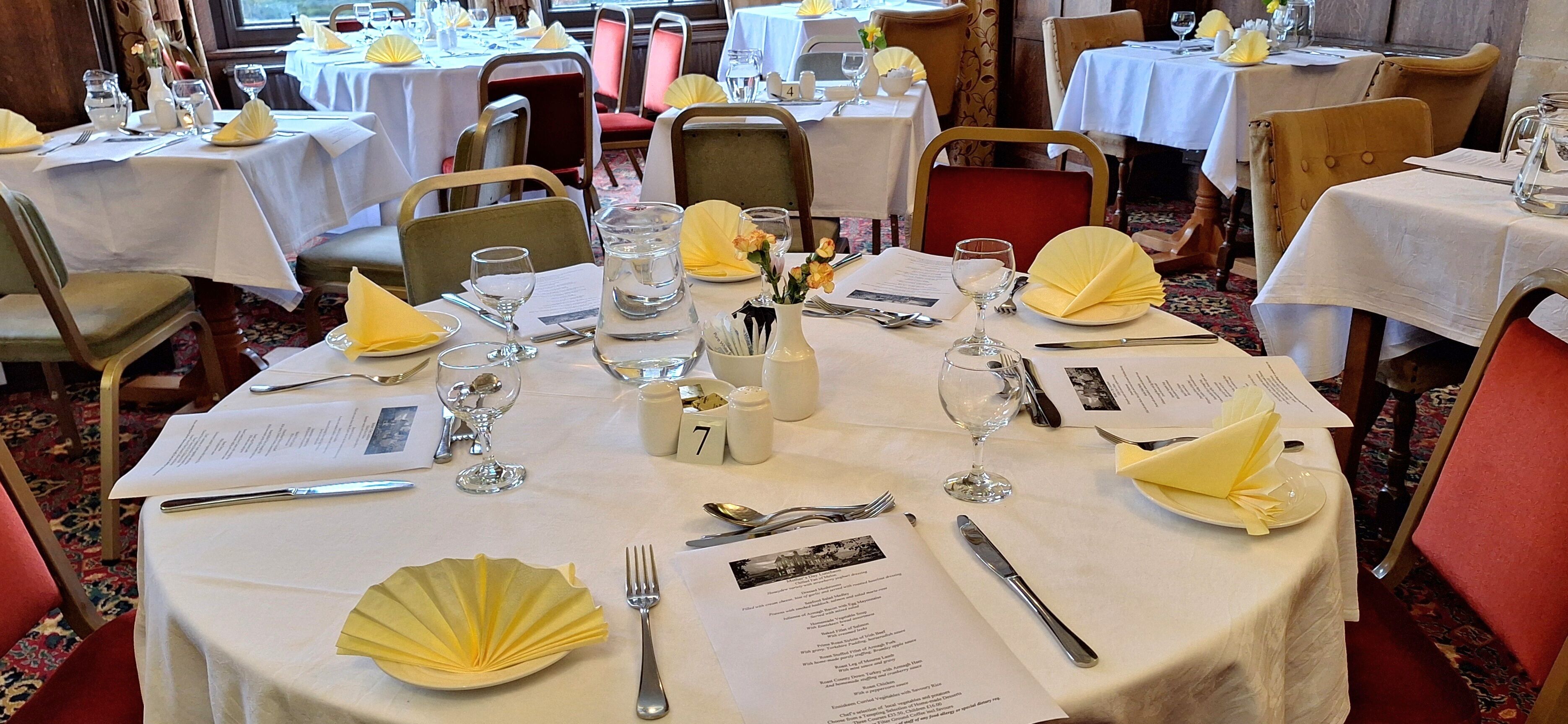 A restaurant with round tables set for dining, each with a menu, cutlery, and a glass of water.