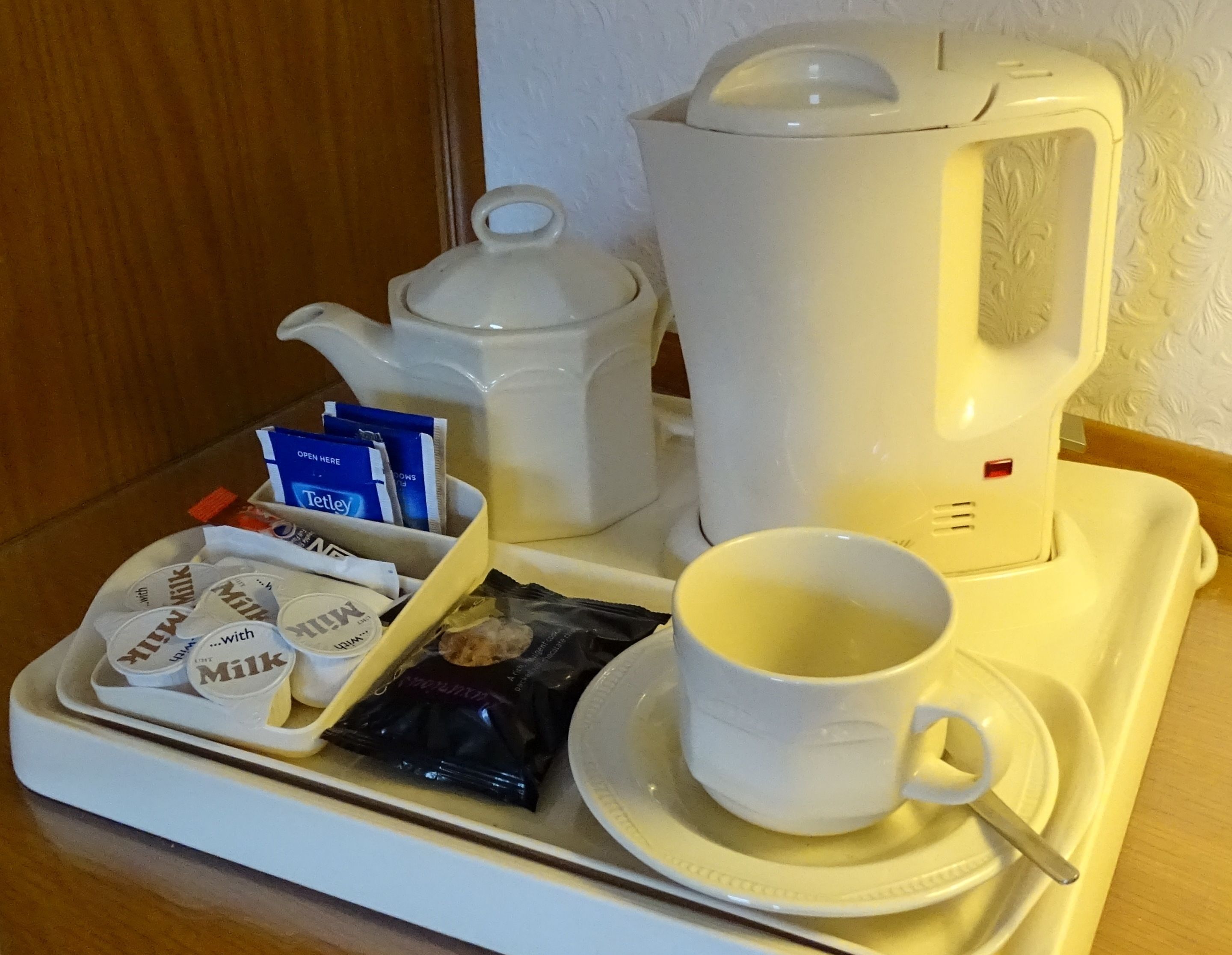 A tray with a teapot, a cup, and packets of milk and tea.