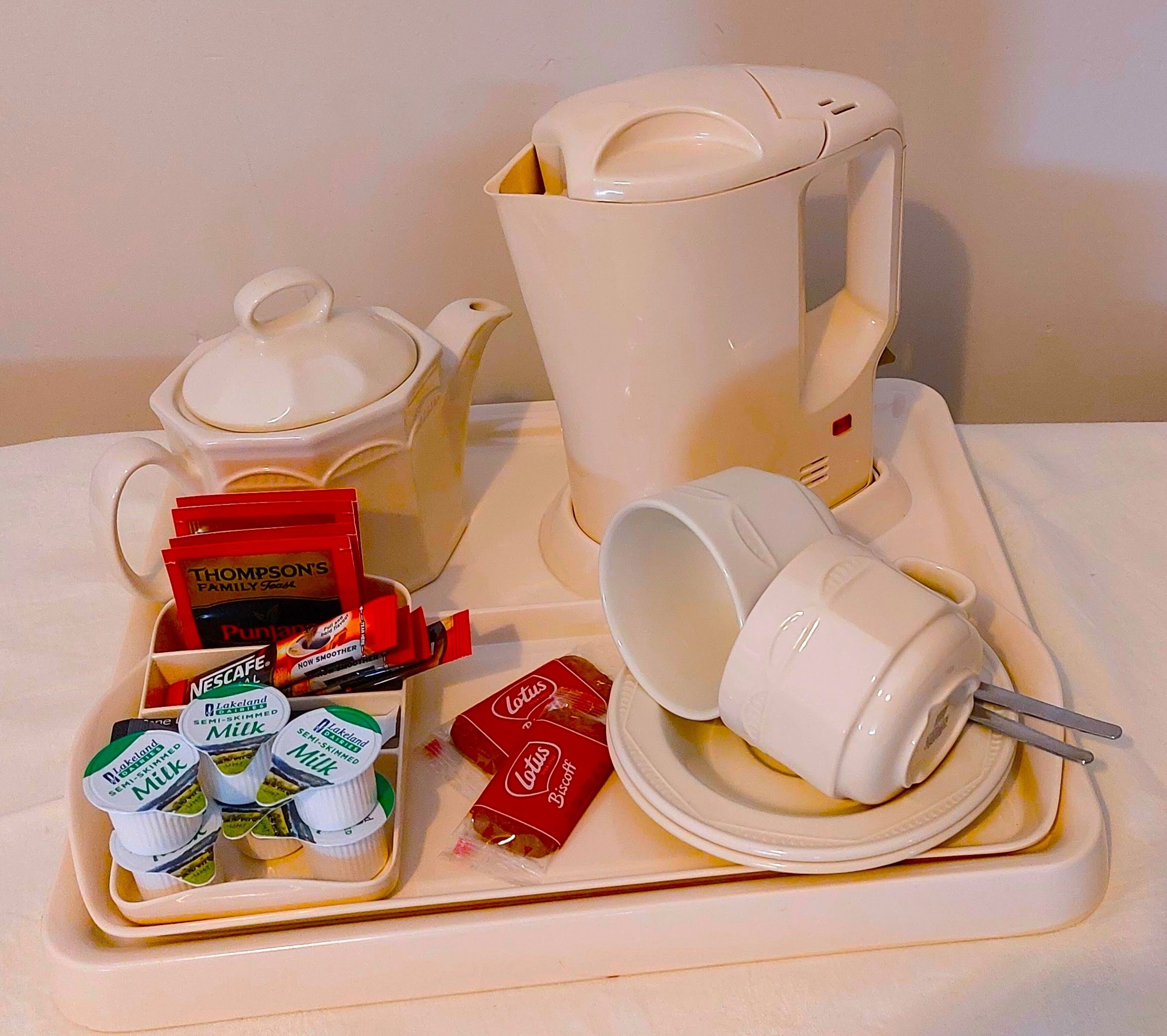 Una bandeja con un hervidor, una taza, una caja de café Nescafé y recipientes con leche.