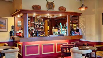 Een bar met een houten toonbank, verschillende zitmogelijkheden en een ruime selectie flessen en glazen.