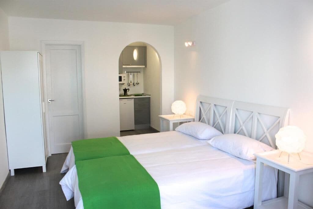 Une chambre d’hôtel comprenant un lit, des tables de chevet, une armoire et une porte en arc donnant sur un coin cuisine.
