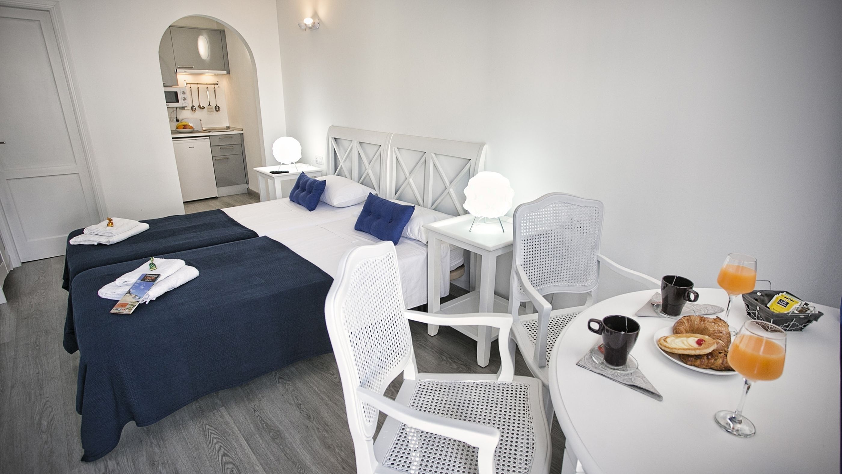 Habitación de hotel con dos camas, una mesa de comedor con desayuno y una kitchenette al fondo.