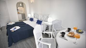 Habitación de hotel con dos camas, una mesa de comedor con desayuno y una kitchenette al fondo.