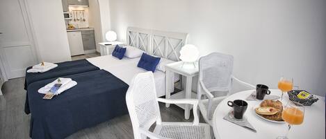 A hotel room with two beds, a dining table with breakfast, and a kitchenette in the background.