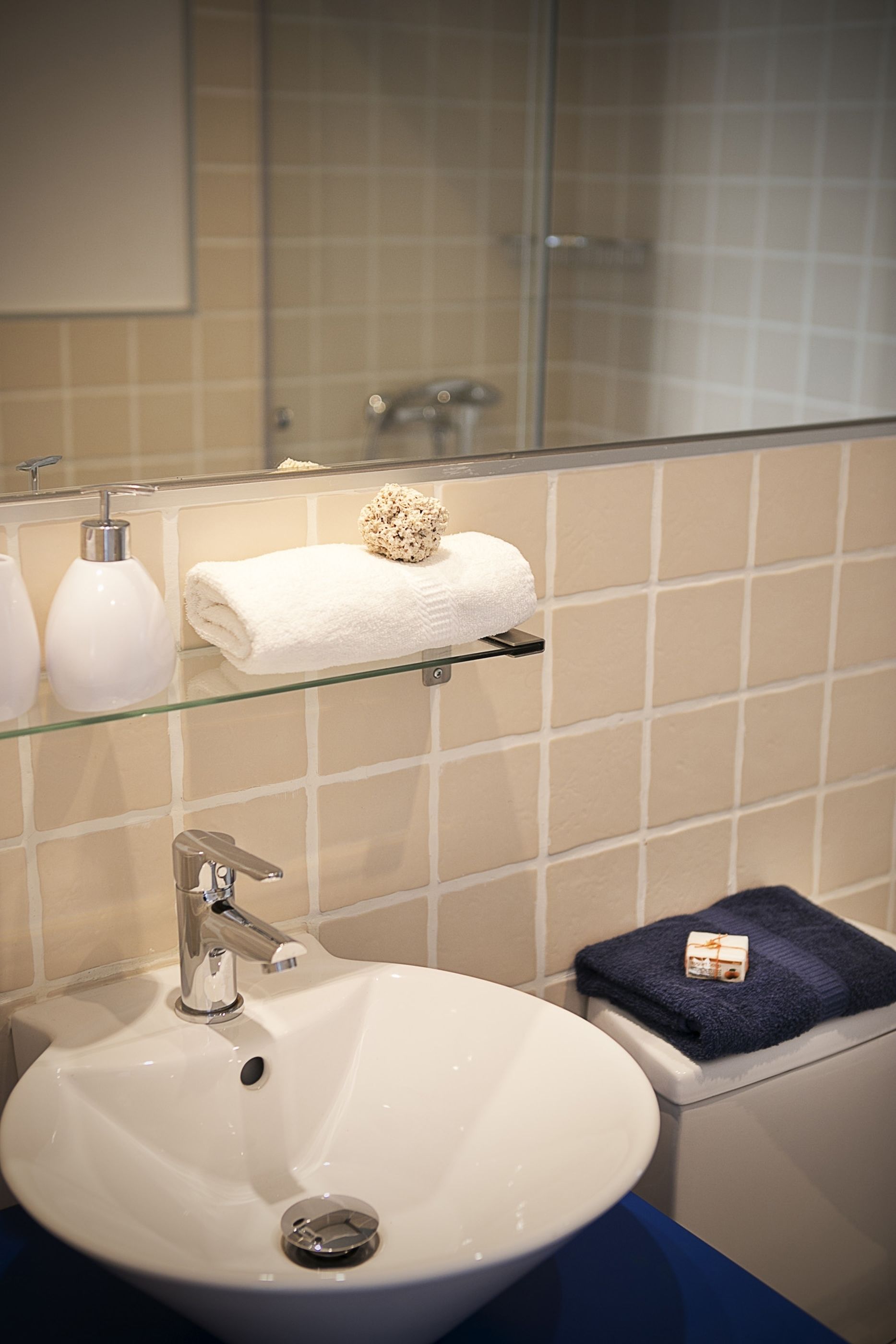 A bathroom with a white sink, a glass shelf with toiletries, and a towel rack.