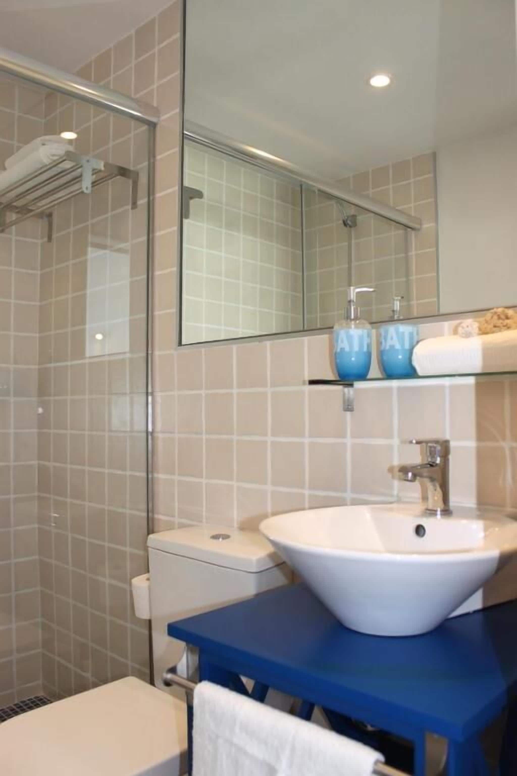 A bathroom with a glass shower enclosure, a white sink, and a blue vanity.