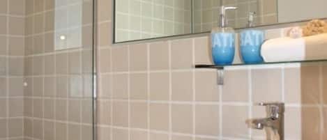 A bathroom with a glass shower enclosure, a white sink, and a blue vanity.
