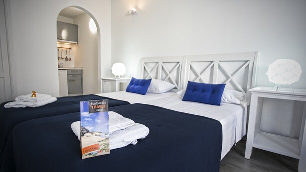 A hotel room with two beds, a travel guide book, and a white wall with a decorative light fixture. - Corralejo Lodge (La Oliva)