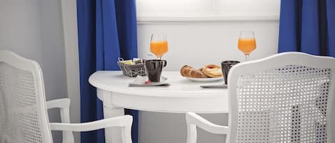A breakfast table with two glasses of orange juice, a croissant, a muffin, and a basket of newspapers.