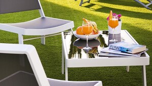 A patio with white lounge chairs, a table with drinks and a book, and a palm tree. - Corralejo Lodge (La Oliva)