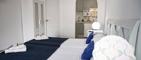 Une chambre d’hôtel avec deux lits, une kitchenette et une porte en arc donnant sur la cuisine.