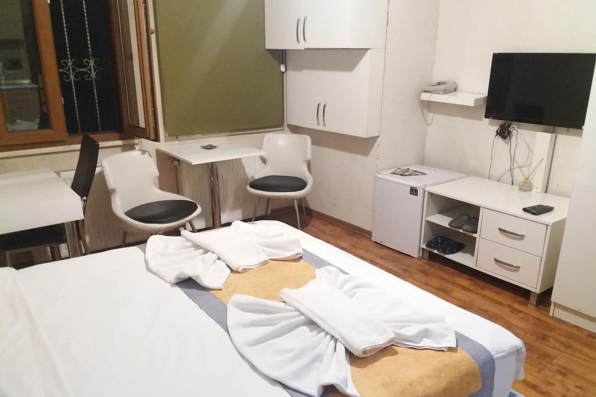 Ein Hotelzimmer mit einem Bett, einem Schreibtisch, zwei Stühlen, einem Fernseher und einem kleinen Schrank.